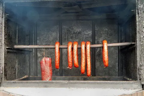 Wędzone kiełbaski i kawałek mięsa wiszące w wędzarni.