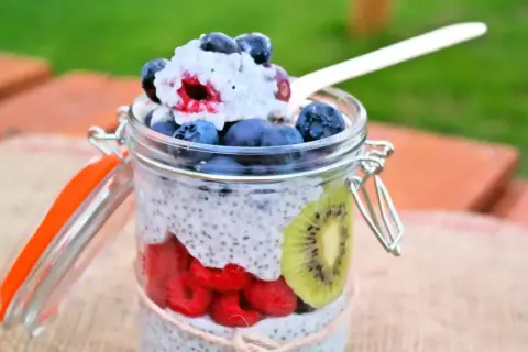 Pudding chia z owocami w słoiku: maliny, borówki, kiwi i łyżka z deserem.