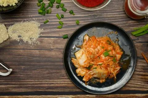 Talerz z kimchi, obok składniki: sezam, czosnek, papryka, szczypiorek, obieraczka i pałeczki.