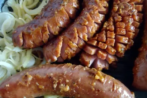 Pyszna kiełbasa grillowa z serem, pokrojona w plastry, podana na cebuli. Idealny przepis na letnie grillowanie!