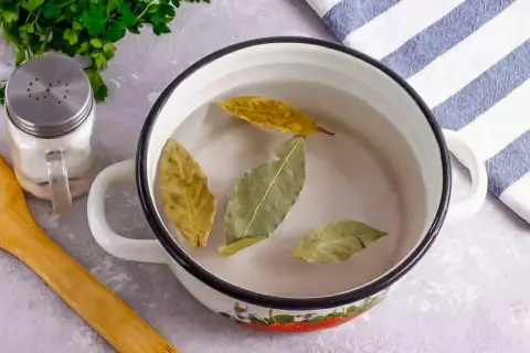 Garnek z wodą i liśćmi laurowymi, obok solniczka i drewniana łyżka.