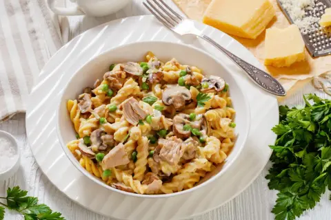 Makaron fusilli z tuńczykiem, groszkiem i pieczarkami w kremowym sosie, udekorowany natką pietruszki.