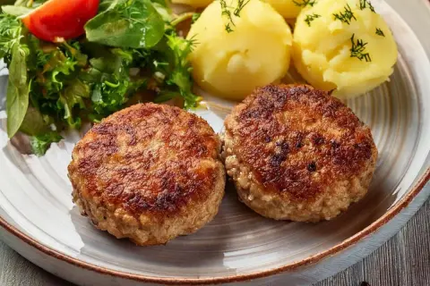 Dwa apetyczne kotlety mielone z airfryer, podane z ziemniakami i świeżą sałatką.