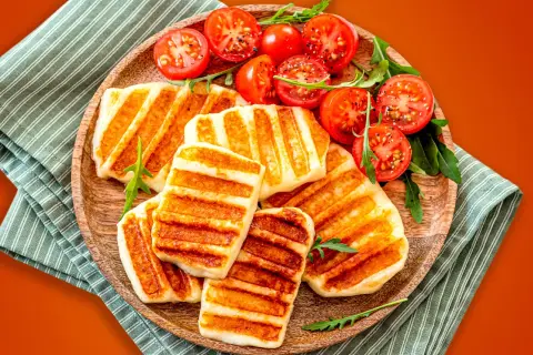 Grillowany ser halloumi z pomidorkami koktajlowymi na drewnianej desce.