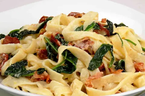 Makaron tagliatelle z kremowym sosem, szpinakiem i kawałkami boczku.