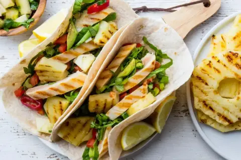 Tacos z grillowanym kurczakiem, ananasem i warzywami, podane z cytryną.