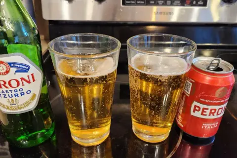 Butelka i puszka Peroni Nastro Azzurro obok dwóch szklanek piwa.