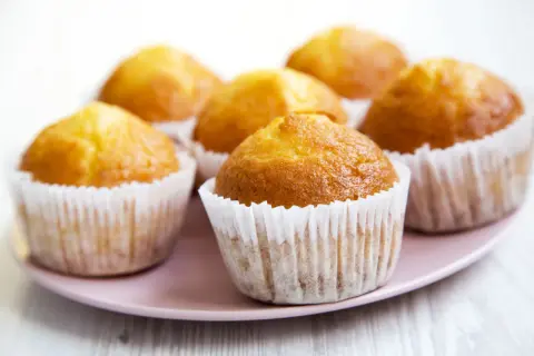 Kilka złotych muffinek w papierowych foremkach na różowym talerzu.