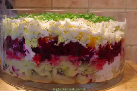 Warstwowa sałatka w szklanej misie: buraki, jajka, ziemniaki, majonez, posypana zieloną pietruszką.