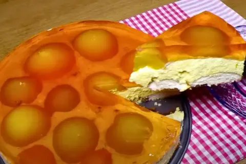Sernik na zimno z brzoskwiniami w galaretce, z wyciętym kawałkiem.