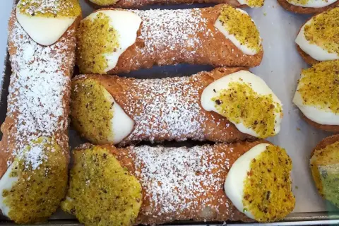 Sycylijskie cannoli z kremem i pistacjami, posypane cukrem pudrem.