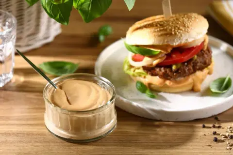 Domowy sos do burgerów w słoiczku obok gotowego burgera na talerzu.