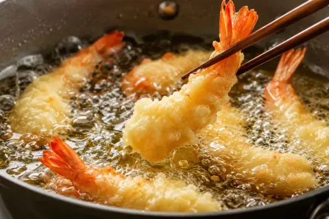 Krewetki w cieście tempura smażące się na złoty kolor w gorącym oleju.