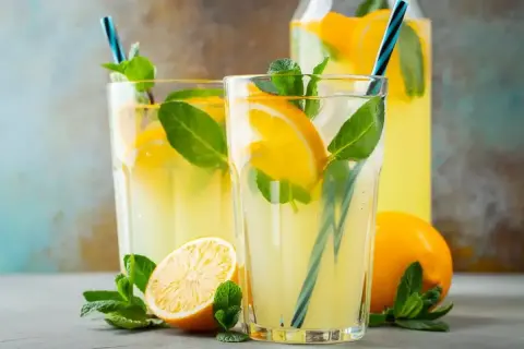 Dwa szklanki orzeźwiającej lemoniady z cytryną i miętą, obok cytryny i dzbanka z napojem.