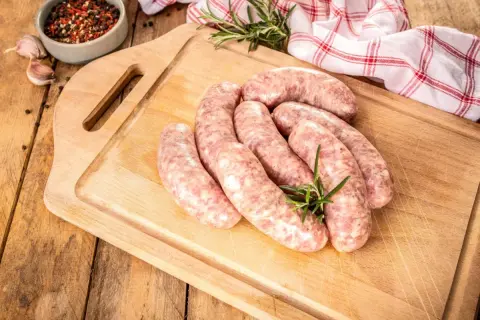 Surowe kiełbaski na desce, obok przyprawy i czosnku. Zastanawiasz się, jak długo parzyć kiełbasę, by była idealna?