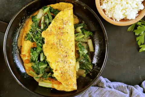 Omlet z serka wiejskiego z zielonymi warzywami na patelni.
