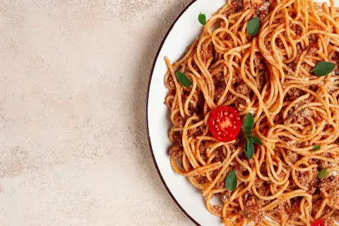 Talerz spaghetti bolognese z pomidorkiem i bazylią. Idealne dodatki do spaghetti, które zachwycą każdego smakosza.
