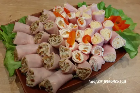 Roladki z szynki z różnymi nadzieniami, ułożone na talerzu z sałatą i papryką.