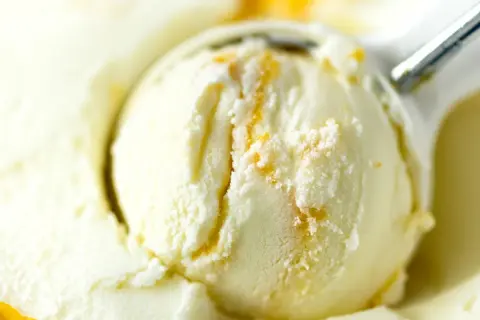 Łyżka do lodów nakłada kremowe lody waniliowe z pomarańczowymi smugami.
