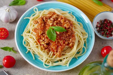 Spaghetti bolognese z mięsnym sosem pomidorowym, udekorowane bazylią, na niebieskim talerzu.