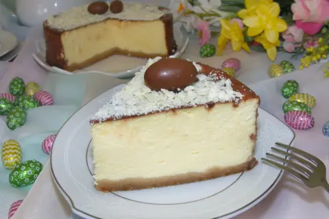 Kawałek kremowego sernika z mascarpone, ozdobiony czekoladowymi jajeczkami i wiórkami białej czekolady, na talerzyku.