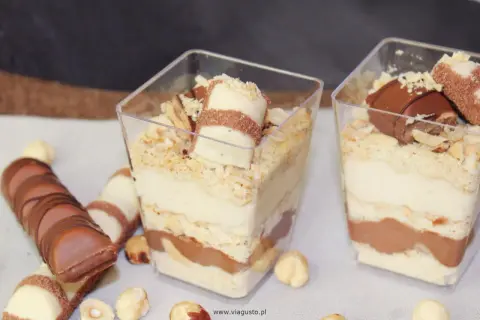 Deser Kinder Bueno w pucharkach z warstwami kremu, ciastek i czekolady, ozdobiony kawałkami batonika i orzechami.