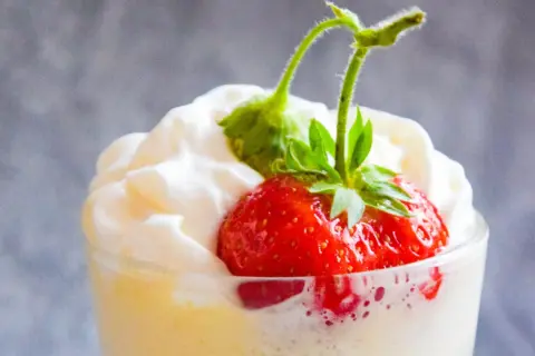 Deser zabaglione z truskawką i bitą śmietaną w szklance.