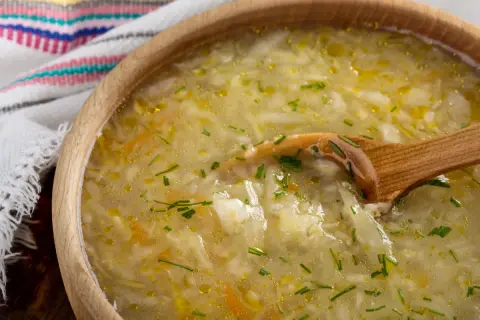 Kapuśniak w drewnianej misce z drewnianą łyżką, ozdobiony szczypiorkiem.