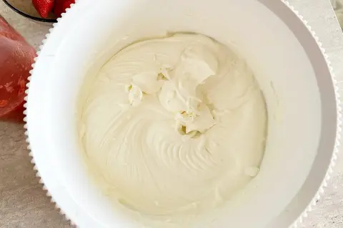 Krem z mascarpone w białej misie, obok miseczka z truskawkami.