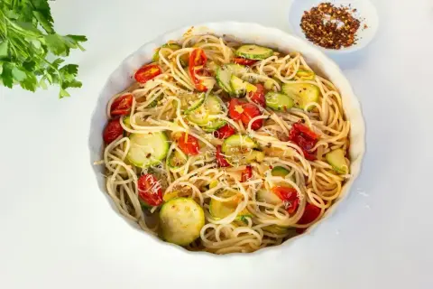 Makaron spaghetti z cukinią i pomidorkami koktajlowymi, posypany parmezanem.