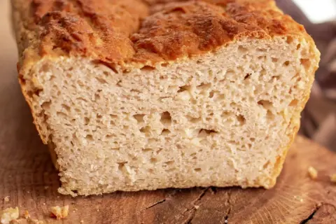 Przekrojony bochenek chleba bezglutenowego na drewnianej desce, z widocznym puszystym wnętrzem.