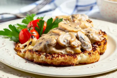 Grillowany kalafior w sosie grzybowym z pomidorkami i natką pietruszki na talerzu.