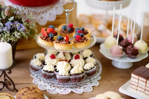 Stół z babeczkami, tartaletkami z owocami, cake pops i ciastem.