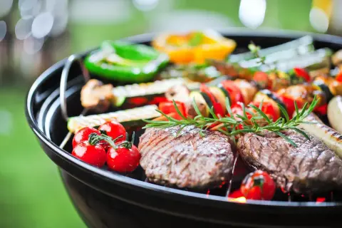 Grill z mięsem, warzywami i ziołami na tle zieleni.
