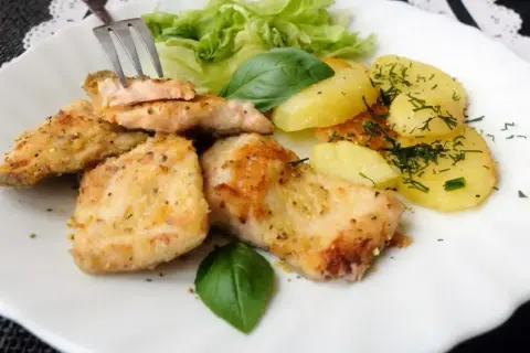 Usmażony pstrąg łososiowy z ziemniakami, sałatą i bazylią na białym talerzu.