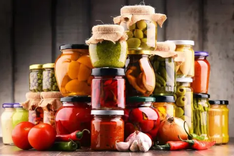 Słoiki z przetworami: warzywa, owoce, oliwki, papryka, pomidory, czosnek, cebula, chili.