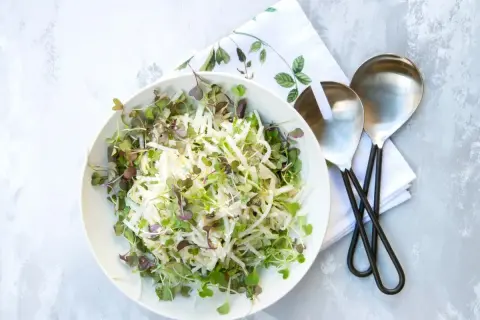 Sałatka coleslaw z kiełkami w białej misce, obok serwetka i łyżki do sałatek.