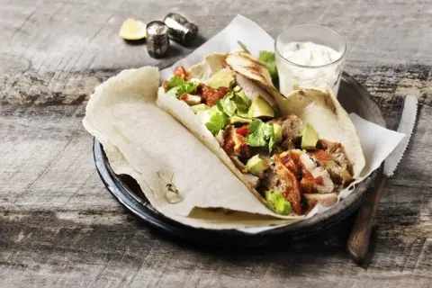 Tortilla z kurczakiem, awokado i sosem na drewnianym stole.