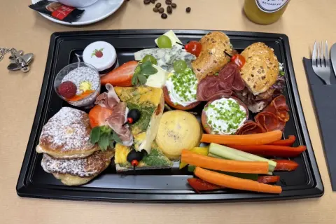 Taca ze śniadaniem kontynentalnym: naleśniki, omlet, sery, wędliny, owoce, warzywa i napój.