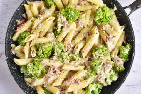 Makaron penne z tuńczykiem i brokułami w kremowym sosie śmietanowo-serowym w czarnej patelni.