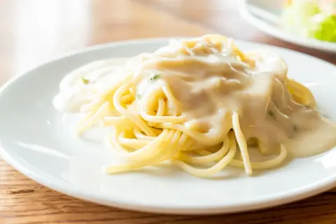 Kremowy sos serowy na makaronie spaghetti na białym talerzu.