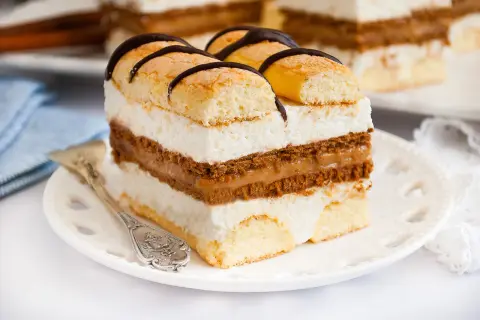 Kawałek ciasta z biszkoptem, kremem mascarpone i karmelem, ozdobiony czekoladą.