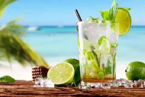 Szklanka orzeźwiającego mojito z limonką i miętą na tle plaży.
