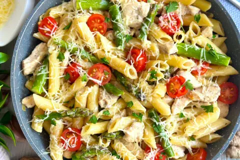 Makaron penne z kurczakiem, szparagami i pomidorkami koktajlowymi, posypany serem.
