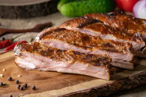 Soczysty, pieczony boczek na desce z przyprawami i papryczkami chili.