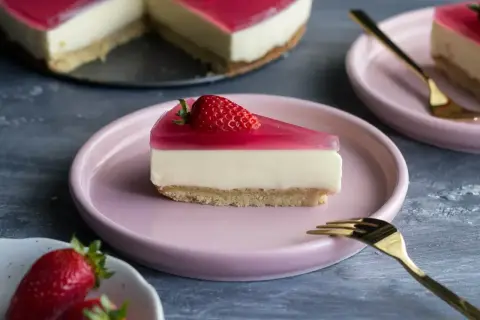 Kawałek sernika z mascarpone i galaretką truskawkową na różowym talerzyku.