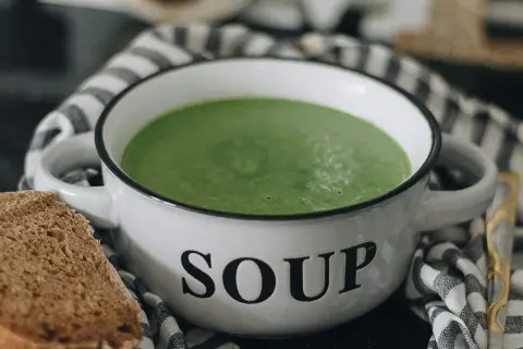 Zielony kremowy zupa w misce z napisem "SOUP". Idealna do mrożenia zup, by cieszyć się smakiem przez cały rok. Obok kromka chleba.