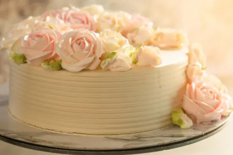 Tort udekorowany kremowymi różami w pastelowych kolorach.