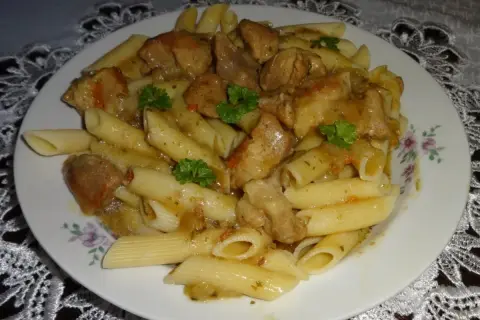 Penne z soczystym makaronem z mięsem wieprzowym w sosie, udekorowane natką pietruszki.