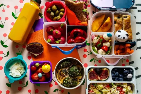 Kolorowy lunchbox z owocami, warzywami, kanapką i napojem.